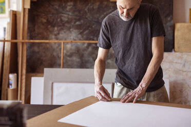 Male artist rubbing on paper in workshop - CAVF16476