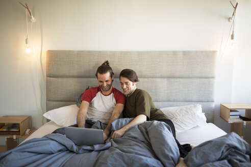 Homosexuelles Paar, das einen Laptop benutzt, während es sich zu Hause auf dem Bett entspannt - CAVF16503