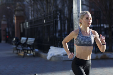 Female athlete running on city street during sunny day - CAVF16531