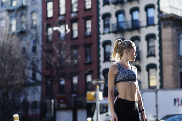 Thoughtful young woman wearing sports bra while listening music against  buildings in city stock photo