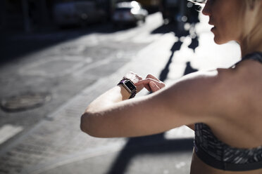 Weibliche Athletin schaut auf die Uhr, während sie auf der Straße steht - CAVF16544