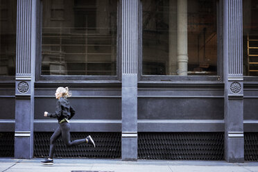 Side view of female athlete running on footpath by building in city - CAVF16547