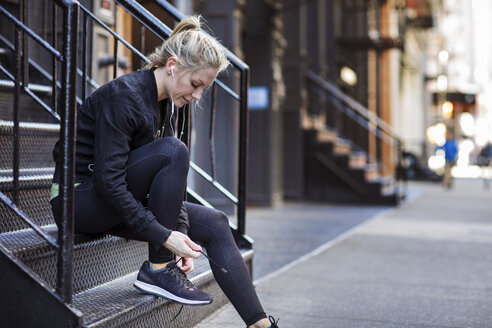 Weibliche Sportlerin bindet Schnürsenkel, während sie auf einer Treppe in der Stadt sitzt - CAVF16548