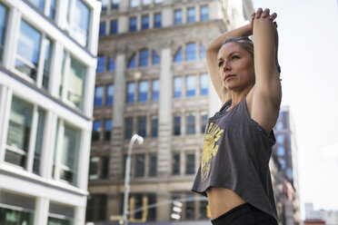 Low angle view of confident athlete stretching hands on city street - CAVF16550