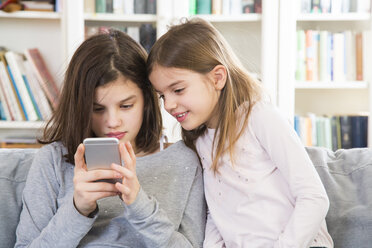 Sisters sitting on couch, using mobile phone - LVF06809