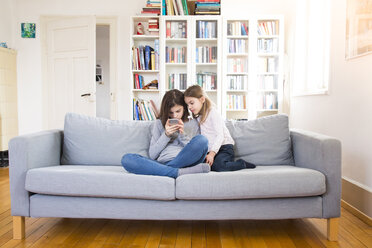 Schwestern sitzen auf der Couch und benutzen ein Mobiltelefon - LVF06810