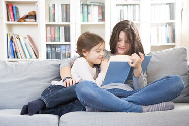 Schwestern sitzen auf der Couch und lesen ein Buch - LVF06811