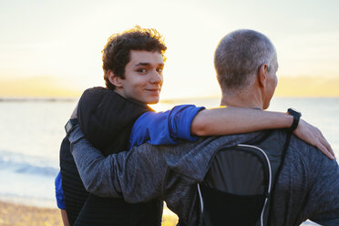 Portrait of confident son with arm around father's shoulder at beach - CAVF16553