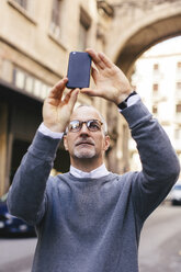 Man photographing with smart phone while standing in city - CAVF16582