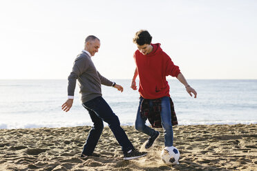 Glücklicher Vater und Sohn spielen Fußball am Strand gegen den klaren Himmel - CAVF16587