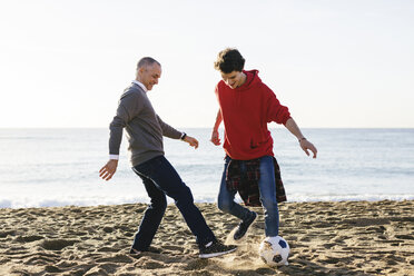 Happy father and son playing soccer at beach against clear sky - CAVF16587