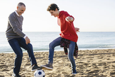 Verspielter Vater und Sohn spielen Fußball am Strand gegen den klaren Himmel - CAVF16588