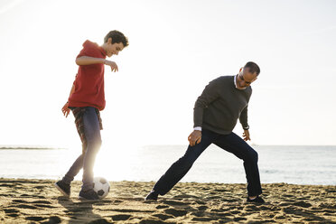 Vater und Sohn spielen Fußball am Strand gegen den klaren Himmel an einem sonnigen Tag - CAVF16590