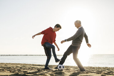 Vater und Sohn spielen Fußball am Strand gegen den klaren Himmel in voller Länge - CAVF16591