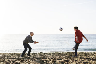 Verspielter Sohn kickt Fußball, während der Vater am Strand gegen den klaren Himmel verteidigt - CAVF16594