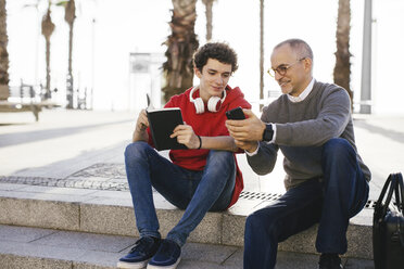 Glücklicher Vater zeigt seinem Sohn das Smartphone, während er auf einer Treppe in der Stadt sitzt - CAVF16599