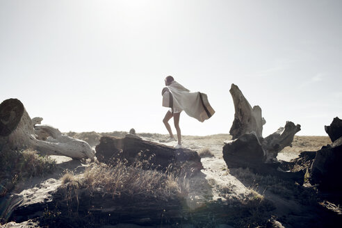 Frau, die an einem sonnigen Tag auf Treibholz am Meer spazieren geht - CAVF16612
