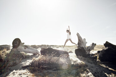 Frau springt an einem sonnigen Tag auf Treibholz - CAVF16614