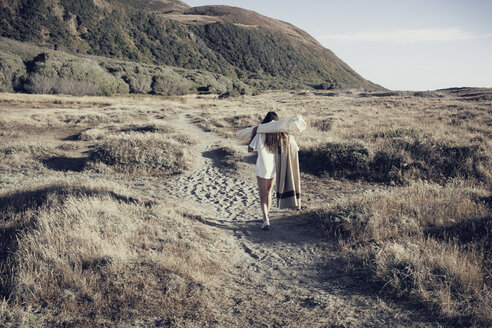Frau trägt Decken bei einem Spaziergang am Meeresufer - CAVF16625