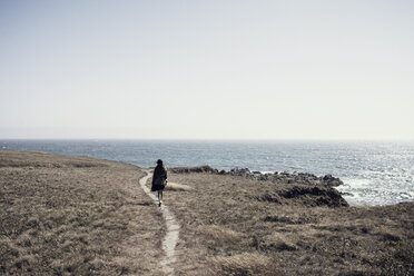 Woman walking on cliff by sea against clear sky - CAVF16636