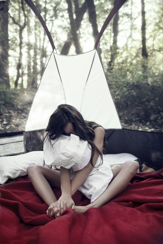 Nackte Frau sitzt mit Kissen auf einem Bett gegen Bäume auf einem Campingplatz, lizenzfreies Stockfoto