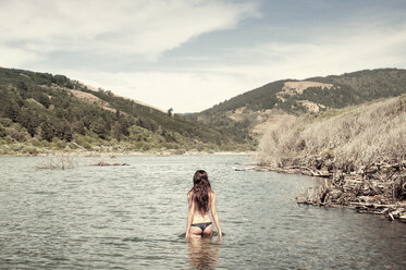 Back view of woman taking off her bikini top while standing in lake stock  photo - OFFSET