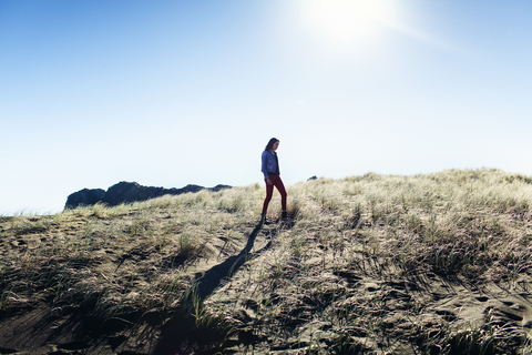 Side view of woman walking on grassy field against clear sky on sunny day stock photo