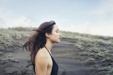 Side view of woman enjoying breeze at Bethells Beach against sky - CAVF16678