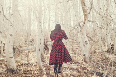 Rückansicht einer Frau, die inmitten kahler Bäume auf einem Feld spazieren geht - CAVF16692