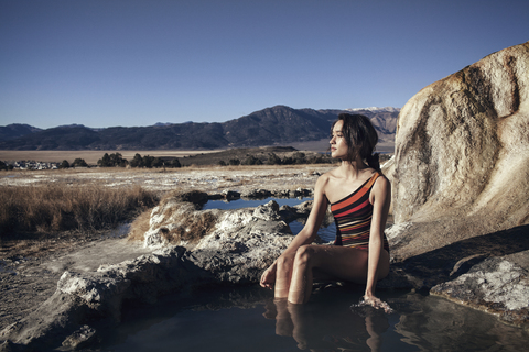 Nachdenkliche Frau entspannt sich in den Bridgeport Hot Springs bei klarem Himmel, lizenzfreies Stockfoto