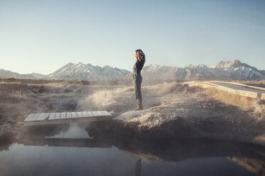 Side view of woman standing on rock at Mammoth Lake Hot Springs against clear sky - CAVF16704