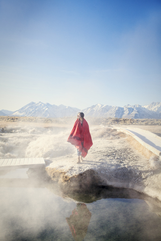 In eine Decke eingewickelte Frau steht auf einem Felsen bei den Mammoth Lake Hot Springs, lizenzfreies Stockfoto