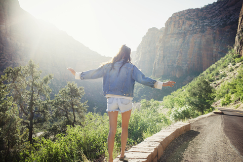 Rückansicht einer Frau, die auf einer Stützmauer an der Straße gegen die Berge läuft, lizenzfreies Stockfoto