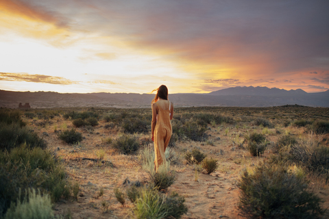 Rear view of woman walking on field against cloudy sky during sunset stock photo