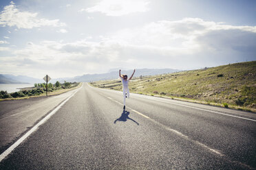 Happy woman running with arms raised on street in sunny day - CAVF16733