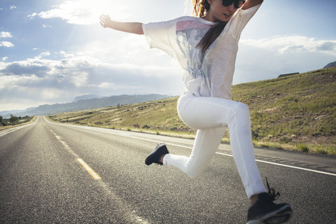 Glückliche Frau springt auf der Straße gegen den Himmel in sonnigen Tag, lizenzfreies Stockfoto