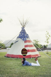 Side view of woman relaxing on grassy field against tent - CAVF16737