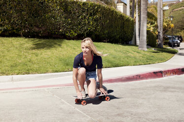 Nachdenkliche junge Frau kniend auf dem Skateboard auf der Straße - CAVF16745