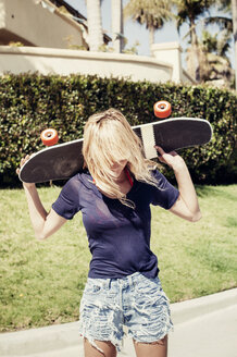 Frau trägt Skateboard auf den Schultern am Fußweg - CAVF16747