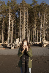 Young woman photographing through smart phone against trees on beach - CAVF16768