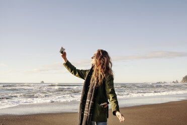 Seitenansicht einer Frau, die am Strand mit ihrem Smartphone fotografiert - CAVF16769