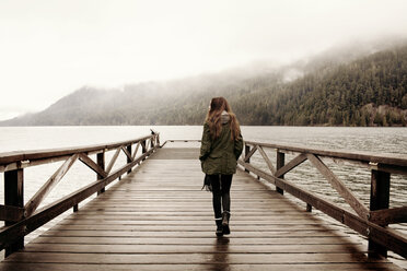 Rear view of woman walking on boardwalk at lake in foggy weather - CAVF16774