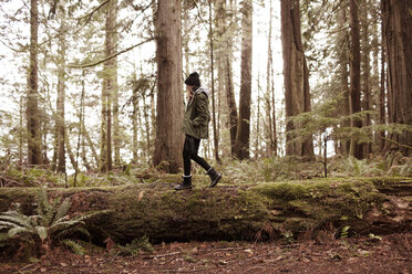 Side view of woman walking on fallen tree in forest - CAVF16777