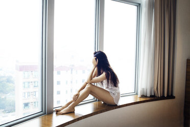 Junge Touristin in Unterwäsche auf der Fensterbank eines Hotelzimmers sitzend - CAVF16779