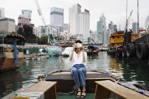 Woman photographing while sitting on boat in city - CAVF16787