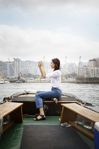 Seitenansicht eines weiblichen Touristen, der auf einem Boot in der Stadt sitzt und fotografiert, lizenzfreies Stockfoto