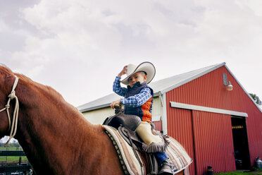 Cute cowboy riding horse against clear sky - CAVF16853