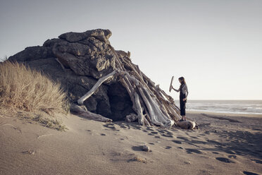 Frau arrangiert Holz auf einer Felsformation am Strand gegen den klaren Himmel - CAVF16866