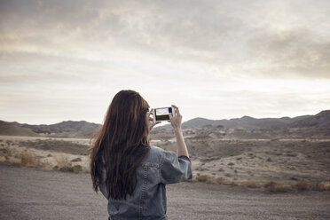 Rückansicht einer Frau, die einen Berg fotografiert, während sie auf einem Feld steht - CAVF16882