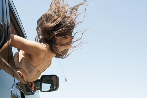 Frau beugt sich aus Autofenster gegen klaren Himmel, lizenzfreies Stockfoto